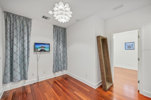 spare room with an inviting chandelier and hardwood / wood-style floors