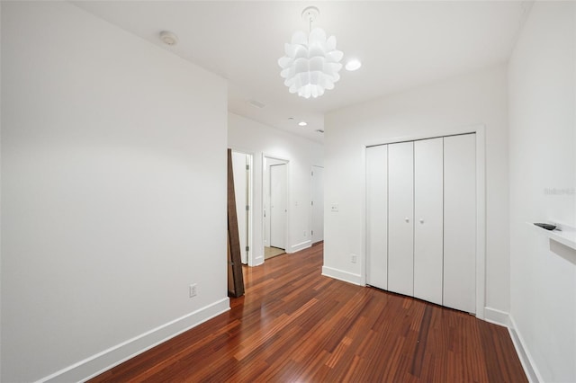 unfurnished bedroom featuring a notable chandelier, a closet, and dark hardwood / wood-style floors