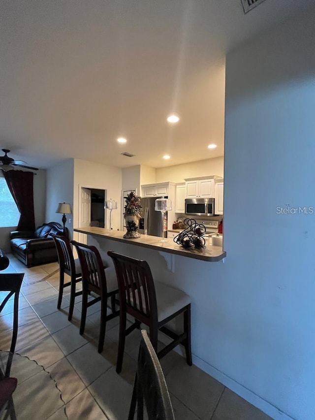 kitchen featuring kitchen peninsula, appliances with stainless steel finishes, a kitchen breakfast bar, ceiling fan, and white cabinetry