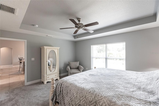 carpeted bedroom with ceiling fan, a raised ceiling, and a textured ceiling