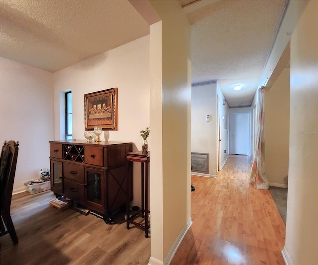 hallway with a textured ceiling and light hardwood / wood-style floors