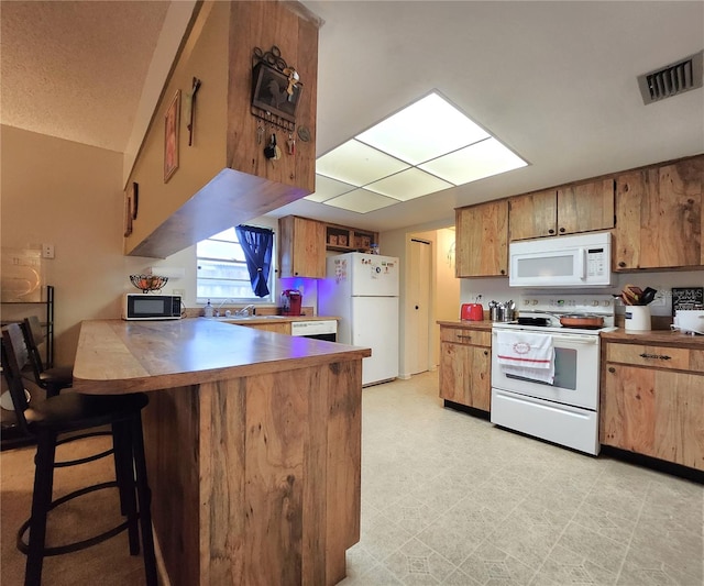 kitchen with sink, a kitchen bar, kitchen peninsula, and white appliances