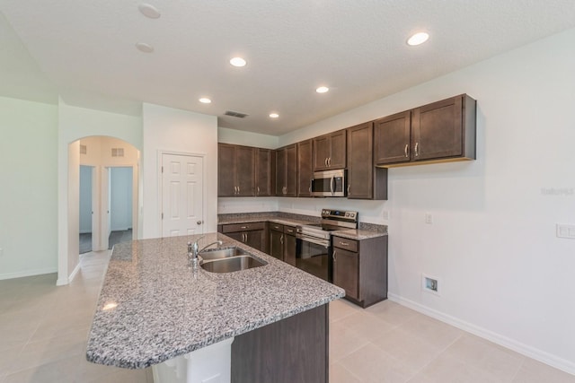 kitchen featuring stainless steel appliances, a kitchen island with sink, sink, and light stone countertops