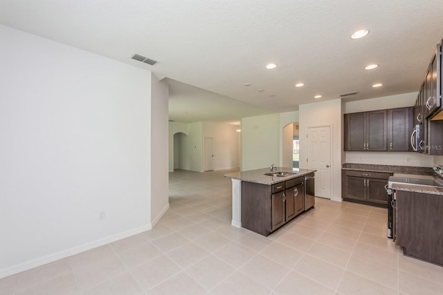 kitchen featuring dark brown cabinets, light stone countertops, appliances with stainless steel finishes, and a center island with sink