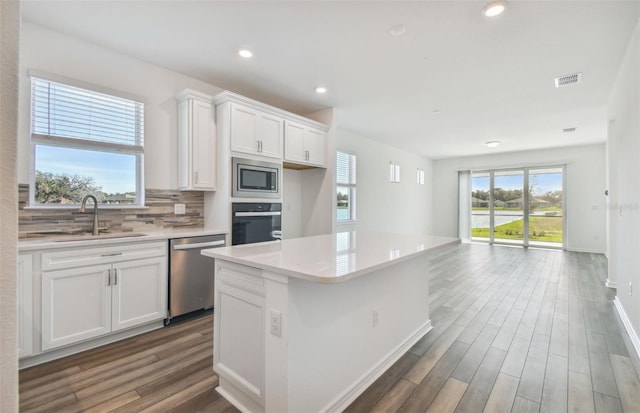 kitchen with sink, appliances with stainless steel finishes, white cabinetry, a center island, and tasteful backsplash