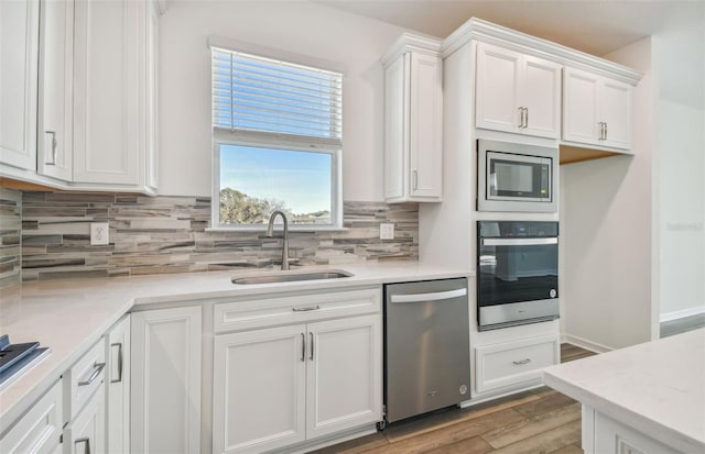 kitchen with sink, appliances with stainless steel finishes, wood-type flooring, white cabinets, and decorative backsplash