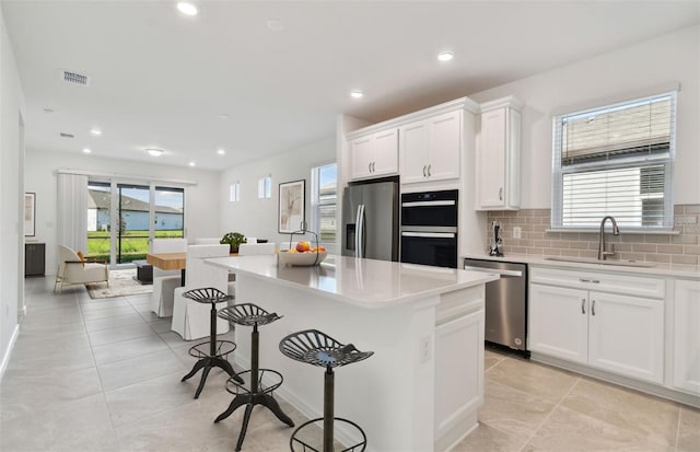 kitchen with stainless steel appliances, a sink, white cabinets, a kitchen breakfast bar, and decorative backsplash