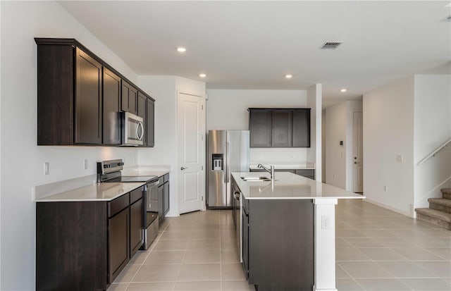 kitchen with stainless steel appliances, an island with sink, dark brown cabinets, and sink