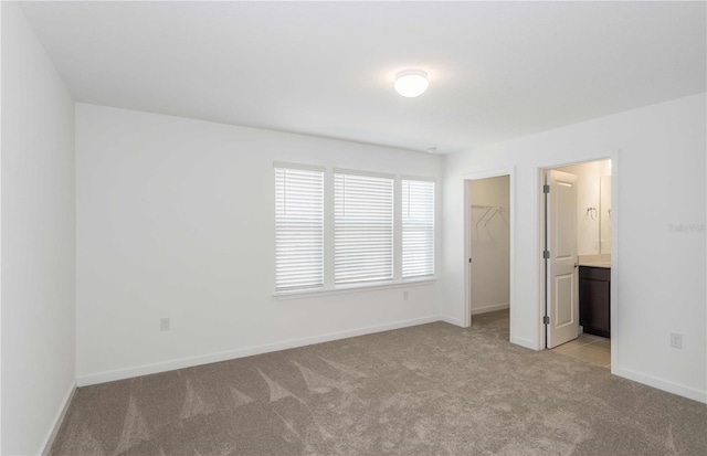 unfurnished bedroom featuring connected bathroom, a spacious closet, light carpet, and a closet