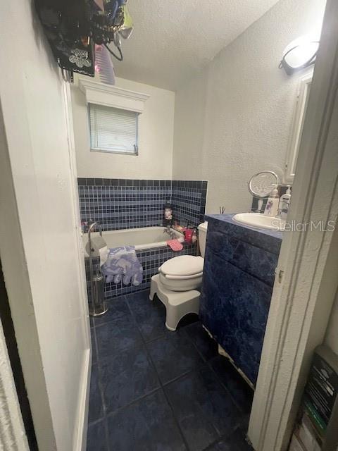 bathroom with vanity, tile patterned floors, toilet, a textured ceiling, and tiled bath