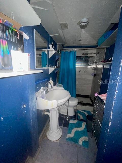 bathroom with toilet, tile patterned flooring, a textured ceiling, and a shower with shower curtain