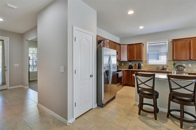 kitchen featuring sink, a breakfast bar area, decorative backsplash, light tile patterned floors, and stainless steel appliances