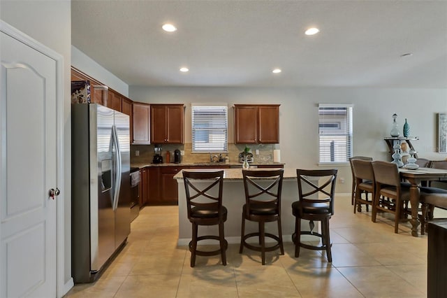 kitchen featuring light tile patterned flooring, a kitchen breakfast bar, stainless steel refrigerator with ice dispenser, decorative backsplash, and a kitchen island