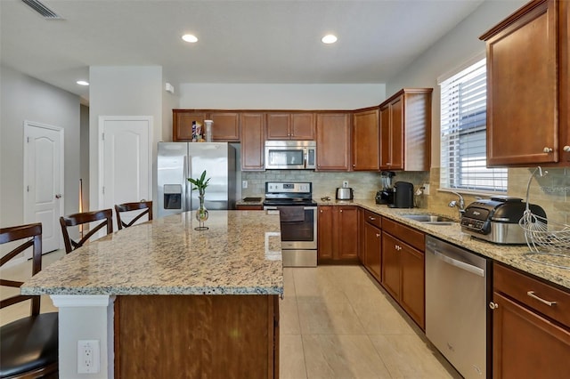 kitchen featuring light stone countertops, a kitchen breakfast bar, stainless steel appliances, sink, and a center island