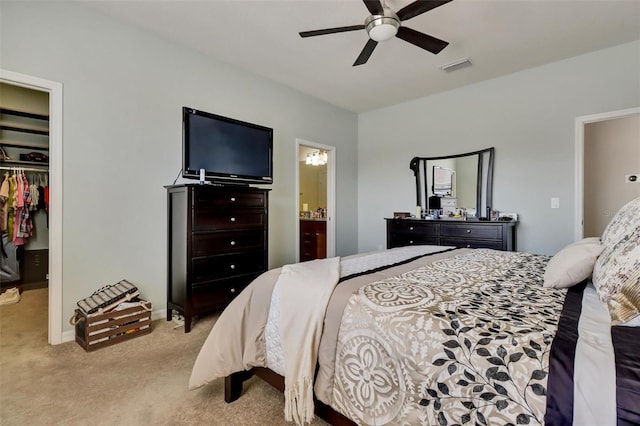 carpeted bedroom featuring a walk in closet, a closet, ensuite bath, and ceiling fan