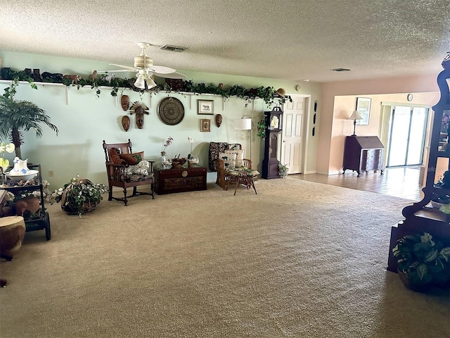 living area featuring carpet floors, visible vents, a textured ceiling, and a ceiling fan