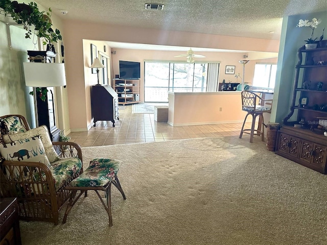 living area with a textured ceiling, a healthy amount of sunlight, light tile patterned floors, and light colored carpet