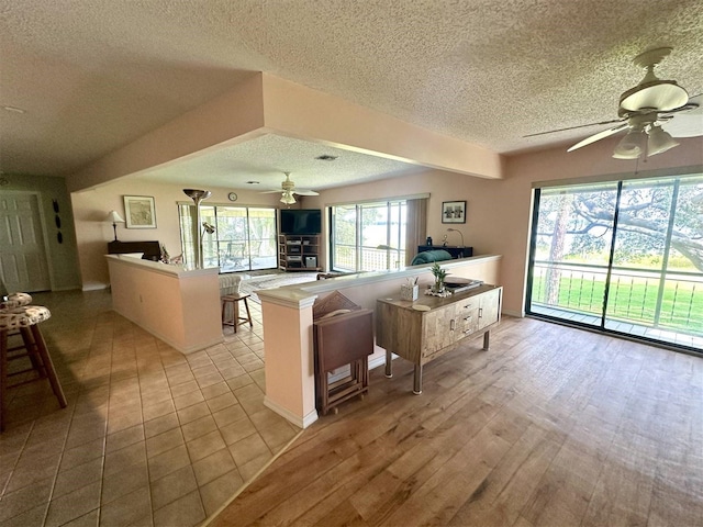 kitchen with open floor plan, ceiling fan, a textured ceiling, light wood-type flooring, and a peninsula