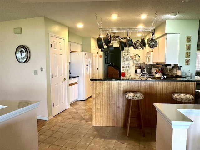 kitchen featuring white appliances, light tile patterned floors, decorative backsplash, a breakfast bar, and a peninsula