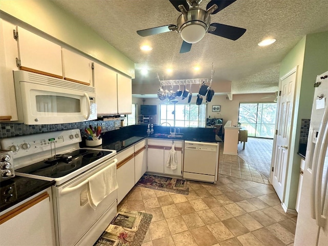 kitchen with white appliances, dark countertops, backsplash, a peninsula, and a sink