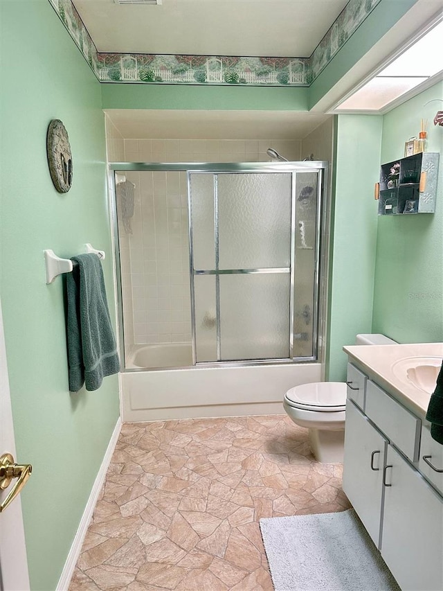 full bathroom with bath / shower combo with glass door, toilet, stone finish flooring, vanity, and baseboards