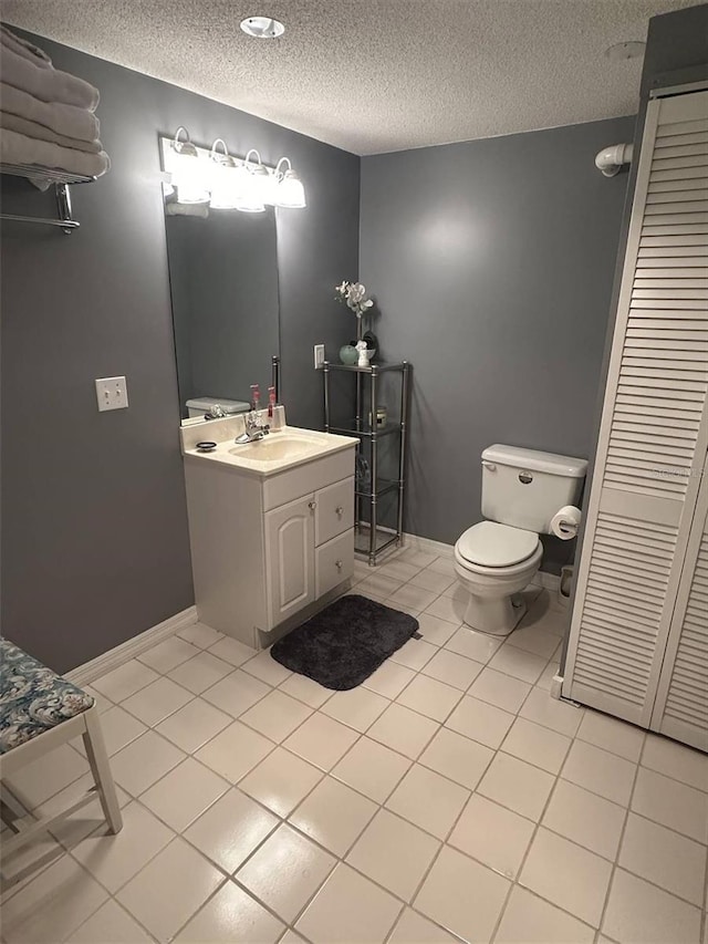 bathroom featuring toilet, vanity, a textured ceiling, tile patterned flooring, and baseboards