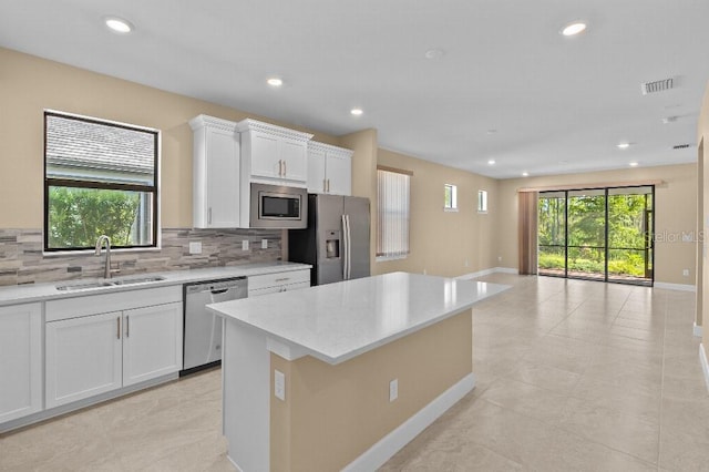 kitchen with sink, stainless steel appliances, backsplash, a center island, and white cabinetry