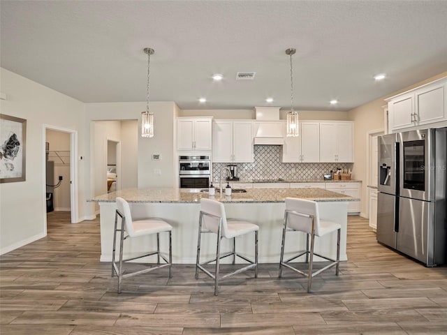 kitchen with stainless steel appliances, white cabinets, a kitchen island with sink, and pendant lighting