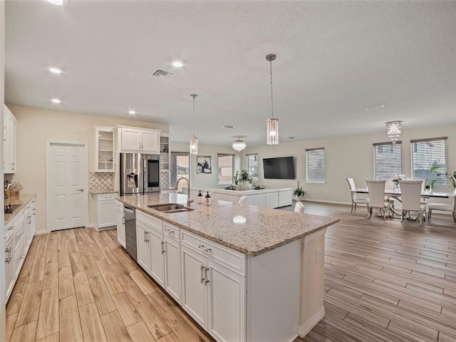 kitchen with stainless steel appliances, white cabinets, sink, and a kitchen island with sink