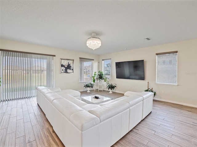 living room with light wood-type flooring, an inviting chandelier, and a wealth of natural light