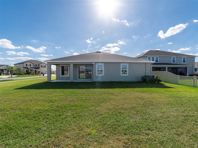 rear view of property featuring a yard, fence, and stucco siding