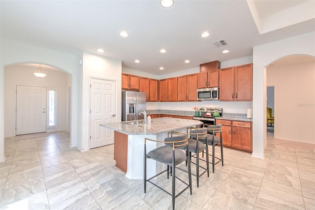 kitchen featuring a kitchen bar, appliances with stainless steel finishes, light stone countertops, sink, and a center island with sink