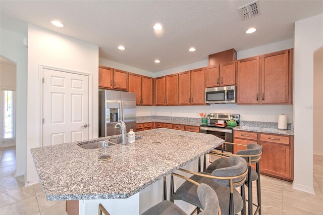 kitchen with sink, stainless steel appliances, light stone counters, a breakfast bar area, and a kitchen island with sink