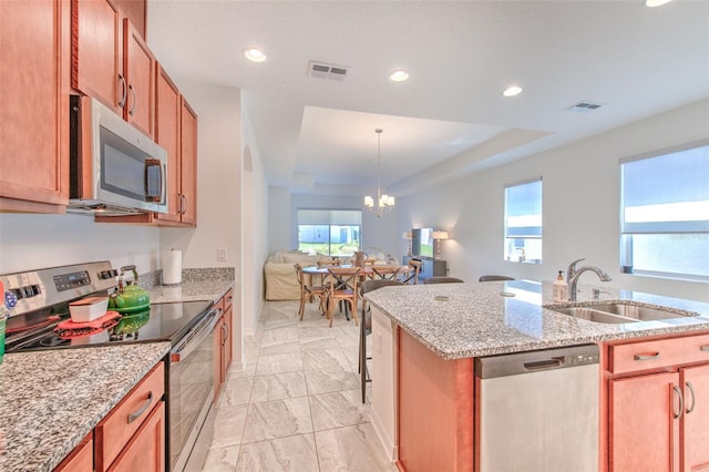 kitchen featuring an inviting chandelier, sink, a tray ceiling, light stone counters, and stainless steel appliances