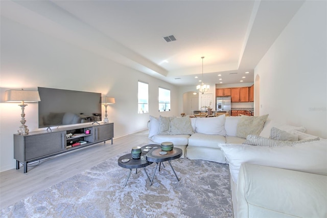 living room featuring light wood-type flooring, a tray ceiling, and a notable chandelier