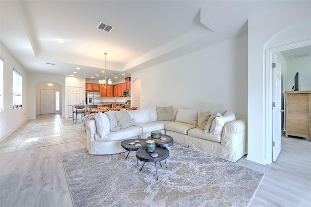 living room featuring a raised ceiling, a notable chandelier, and light wood-type flooring