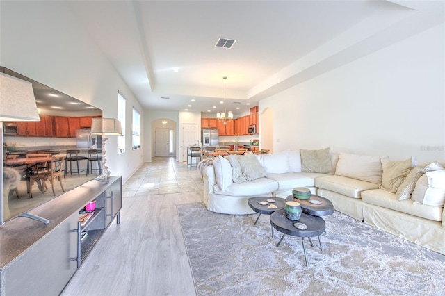 living room featuring a notable chandelier, light hardwood / wood-style floors, and a tray ceiling