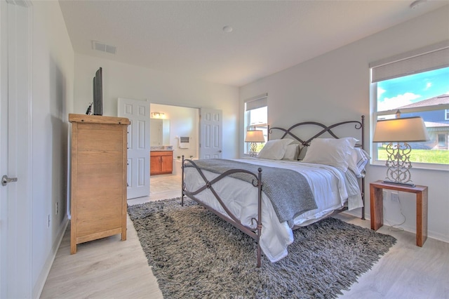 bedroom with connected bathroom and light hardwood / wood-style flooring