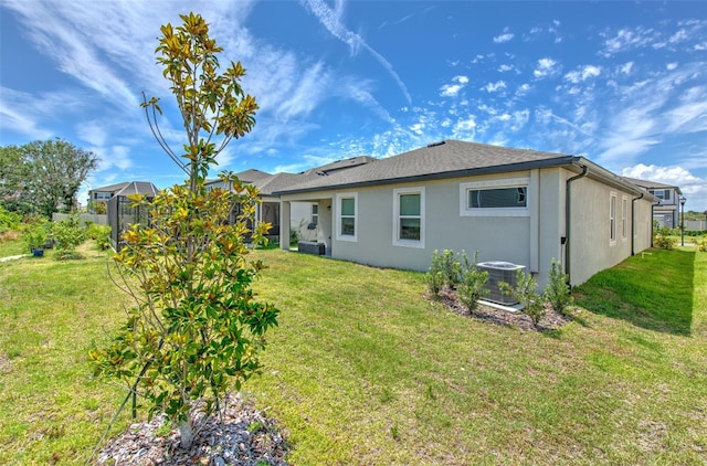 rear view of property with a lawn, glass enclosure, and central air condition unit