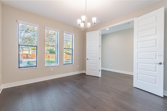 spare room featuring dark wood-type flooring, a chandelier, and baseboards