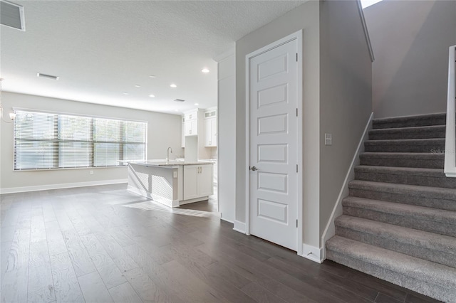 staircase featuring baseboards, a textured ceiling, visible vents, and wood finished floors