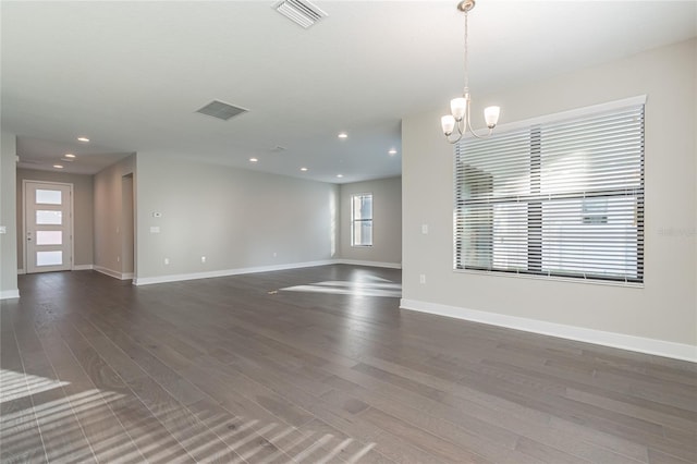 empty room featuring dark wood-style flooring, visible vents, a notable chandelier, and baseboards