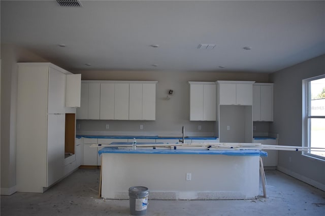 kitchen featuring visible vents, a kitchen island with sink, and white cabinetry