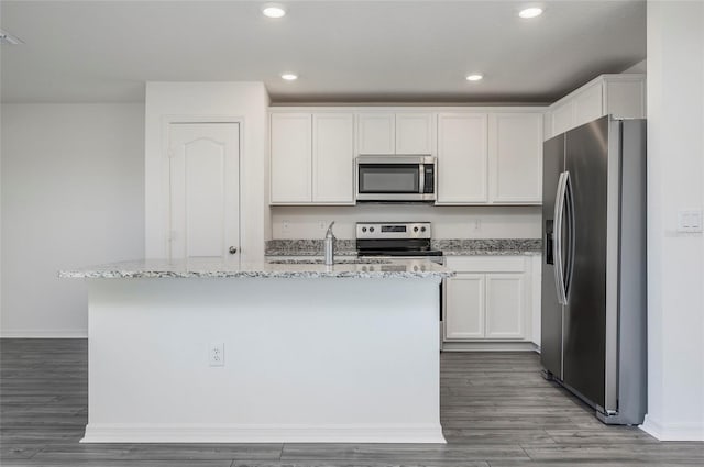 kitchen with a kitchen island with sink, hardwood / wood-style flooring, stainless steel appliances, light stone countertops, and white cabinets