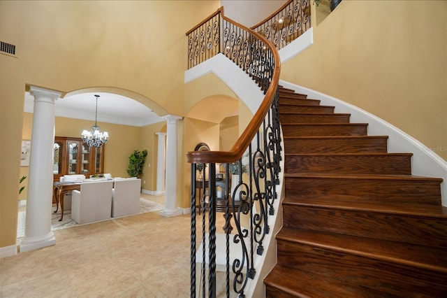 stairway featuring crown molding, a towering ceiling, and ornate columns