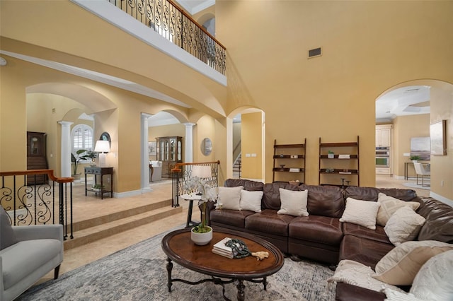 living room with a towering ceiling, ornate columns, and light tile floors