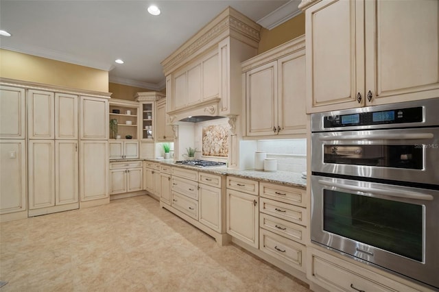 kitchen featuring crown molding, cream cabinets, light stone counters, backsplash, and appliances with stainless steel finishes