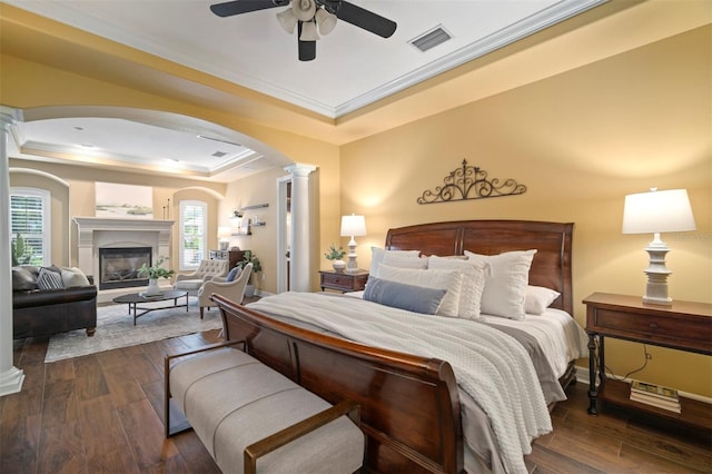 bedroom featuring ceiling fan, a tray ceiling, decorative columns, and dark hardwood / wood-style flooring