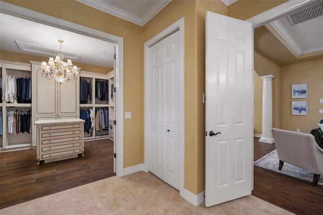 hallway with a notable chandelier, ornamental molding, decorative columns, and wood-type flooring