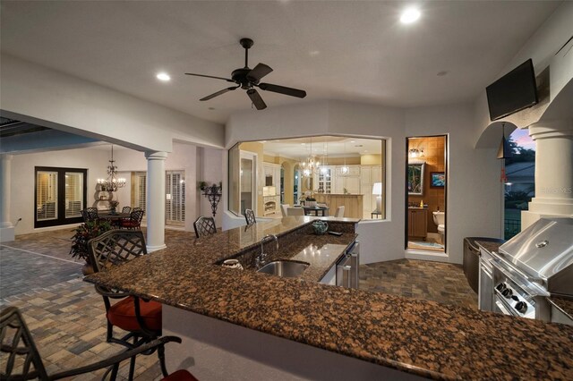 kitchen featuring decorative columns, pendant lighting, ceiling fan with notable chandelier, dark tile flooring, and sink